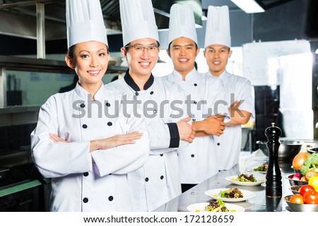 Asian Indonesian and Chinese chefs along with other cooks in restaurant or hotel commercial kitchen cooking, finishing dish or plate