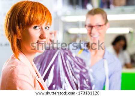 Customer collecting clothes in laundry shop or textile dry-cleaning packed in bag with hanger