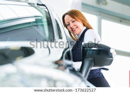 Young woman beside a new car in car dealership, obviously she is buying the auto, or making a test drive