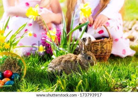 Living Easter bunny with eggs in a basket on a meadow in spring, children in the background