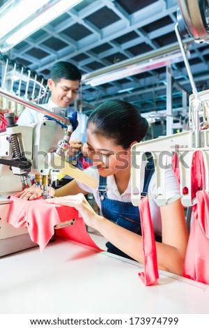 Asian Seamstress or worker in a textile factory sewing with a industrial sewing machine, she is very accurate, the manager looking pleased at her work