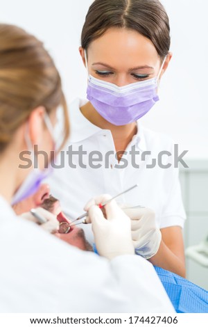 dentist in her practice or office treating male patient with assistant wearing masks and gloves