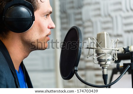Young male singer or musician with microphone and headphone for audio recording in the Studio