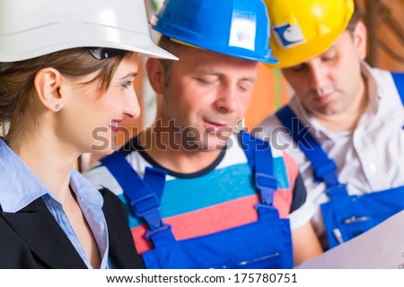 Construction site team or architect and builder or worker with helmets controlling or having discussion of plan or blueprint
