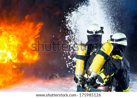 Firefighter - Firemen extinguishing a large blaze, they are standing with protective wear in front of wall of fire