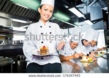 Asian Indonesian chef along with other cooks in restaurant or hotel kitchen cooking, finishing  dish or plate for dessert