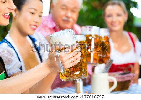 In Beer garden - friends in Tracht, Dirndl and Lederhosen drinking a fresh beer in Bavaria, Germany