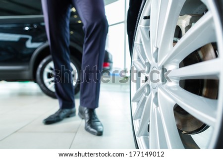 Seller or car salesman in car dealership presenting the extra decorations like sport rims of his new and used cars in the showroom