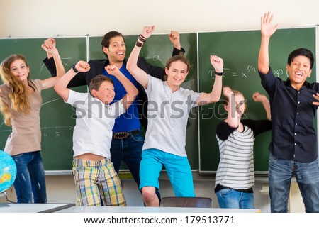 Successful Teacher and students jump in front of a blackboard with math work in a classroom or class school while lesson