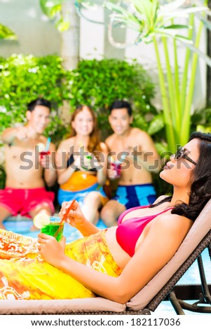 Asian friends partying and drinking fancy cocktails at hotel or club pool party