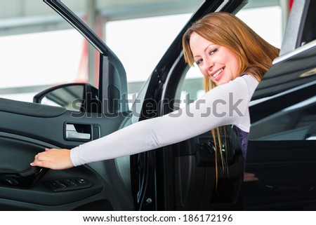 Young woman sits in new car on driver seat in a car dealership, obviously she is buying the auto
