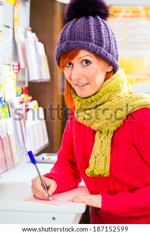 Young woman in a Lotto store playing lottery ticket to win with luck, she fills the ticket with a pen