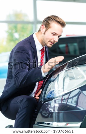 Seller or car salesman in car dealership presenting the reflecting car paint of his new and used cars in the showroom