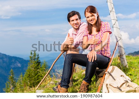 Hiking - Young couple sitting on mountain summit at cross in the Bavarian Alps and enjoys the panorama in the leisure time or in vacation