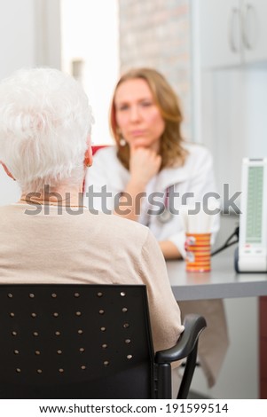 Young female doctor sitting with pensioner in surgery consultation hour at desk