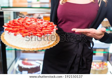 Female confectioner presenting tray of cake in bakery or pastry shop