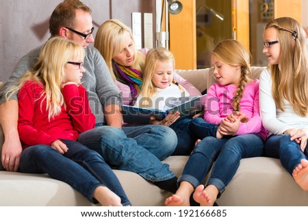 Family sitting together with mother, father and children comfortable on sofa, listening to fairy tale from story book