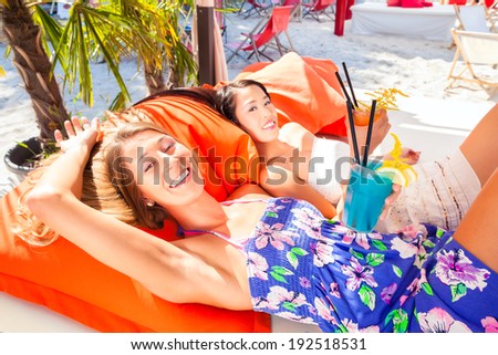 Girls in sound loungers at beach bar with drinks