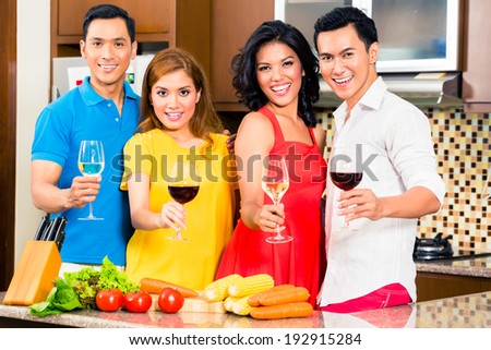 Asian friends cutting vegetables cooking together in domestic kitchen for dinner party, drinking wine