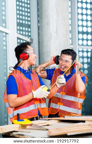 Asian Indonesian builder or craftsman and supervisor with ear or hearing protection and glasses on a tower building or construction site