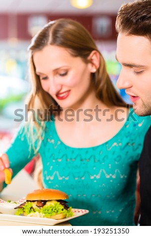 Friends or couple eating fast food with burger and fries in American fast food diner