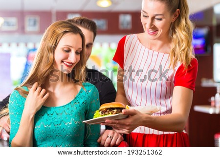 Friends or couple eating fast food in American fast food diner, the waitress wearing a short costume