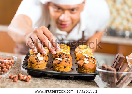 Asian man baking homemade cup cake muffins in his kitchen for dessert