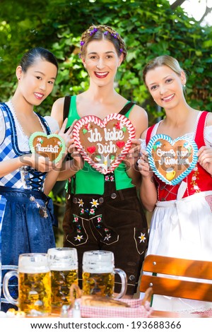 Young women in traditional Bavarian clothes or tracht with a gingerbread souvenir heart in beergarden on Oktoberfest