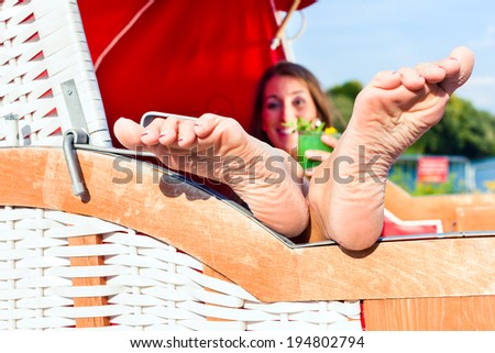 Young woman relaxing in  wicker bench chair of  beach bar and drinking cocktail