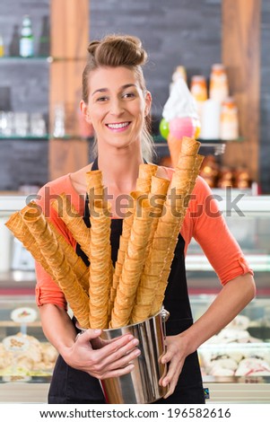 Young saleswoman in an ice cream parlor with many cones for ice cream cornets