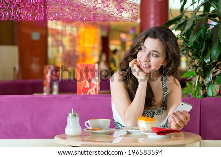 Young woman in a cafe or ice cream parlor eating a cake and using her phone, maybe she is single or waiting for someone