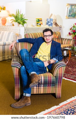 Young man testing and buying armchair in furniture store