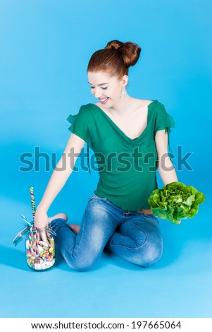 Young woman with healthy and unhealthy food like salad and candy in studio
