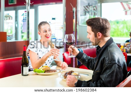 Young couple eating fast food and drinking red wine in a American retro fast food diner