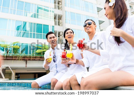 Friends sitting by swimming pool with drinks