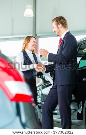 Seller or car salesman and customer in dealership, they shaking hands, hands over the car keys and seal the purchase of the auto or new car