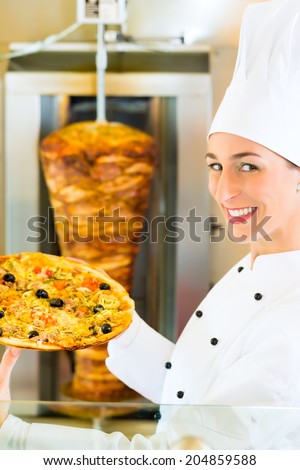 Doner kebab - friendly female vendor in a Turkish fast food eatery, holding a pizza in front of skewer