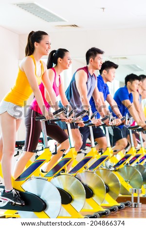 Chinese Asian sport group of men and women in fitness club or gym exercising on spinning bikes
