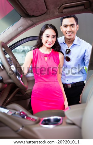 Asian couple choosing luxury car in auto dealership looking at the interior