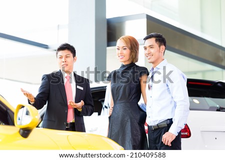Asian couple buying car in auto dealership consulting the salesman