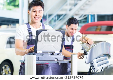 Asian Chinese car mechanics checking auto engine with diagnostics tool in his workshop
