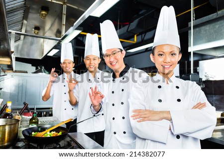 Asian Indonesian chefs along with other cooks in restaurant or hotel kitchen cooking or fry with a pan at the stove
