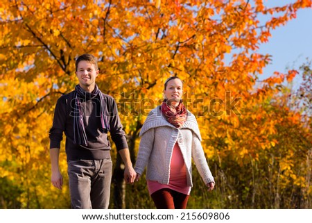 Young family or couple or man and pregnant woman walking through colorful trees in fall or autumn