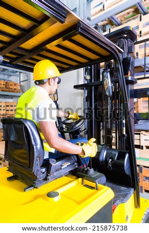 Asian fork lift truck driver lifting pallet in storage warehouse