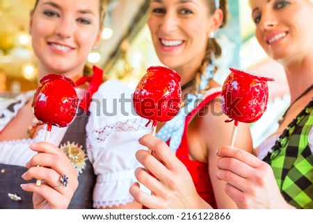 Friends visiting together Bavarian fair in national costume eating candy apple