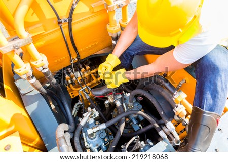 Asian motor mechanic working on construction or mining machinery in vehicle workshop