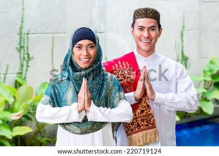 Asian Muslim man and woman welcoming guests wearing traditional dress