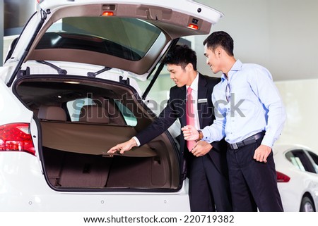 Car salesman in Asian dealership showing trunk of SUV car to customer