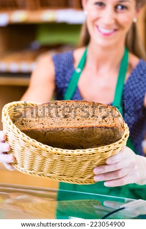Female baker at organic supermarket bakery offering customer bread