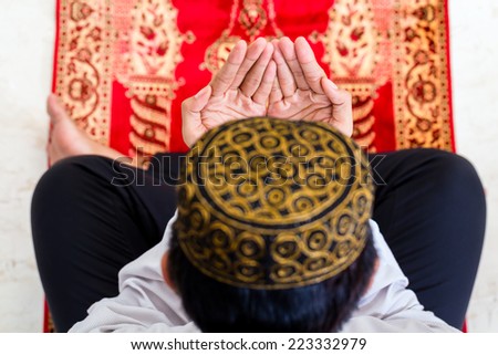 Asian Muslim man praying on carpet wearing traditional dress Asian Muslim man praying on carpet wearing traditional dress